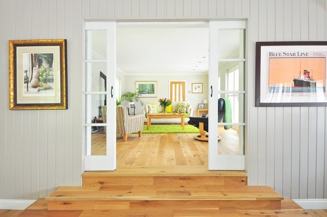 Schody a dveře do obývacího pokoje, kde je sedací souprava, křesla, stůl a obrazy